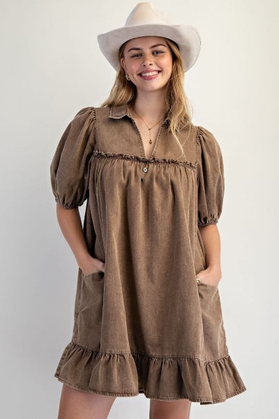 Woman wearing a brown dress with puff sleeves and a white hat on a plain background