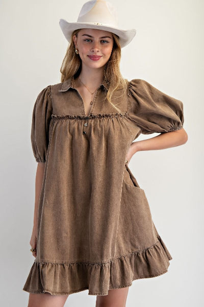 Woman wearing a brown dress with puffed sleeves and a white hat on a plain background