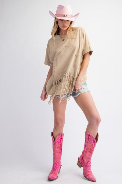 Person wearing a beige fringe poncho, denim shorts, and pink cowboy boots on a white background