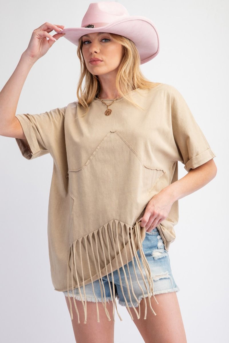 Woman wearing a beige fringe top, denim shorts, and a pink cowboy hat on a white background