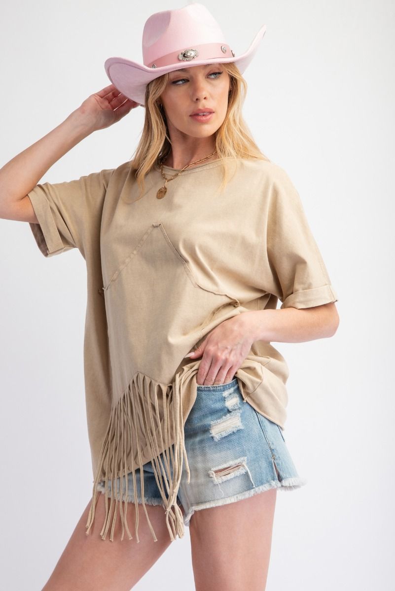 Woman wearing a beige fringe top, denim shorts, and a pink cowboy hat on a white background