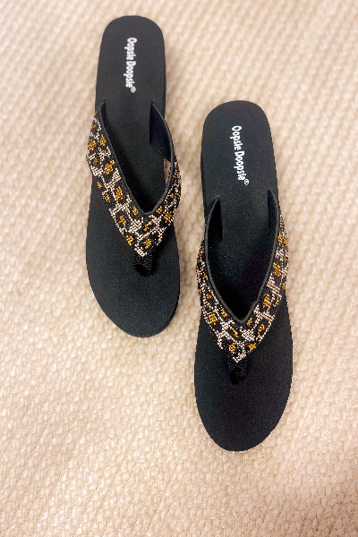 Black sandals with decorative straps on a textured beige surface