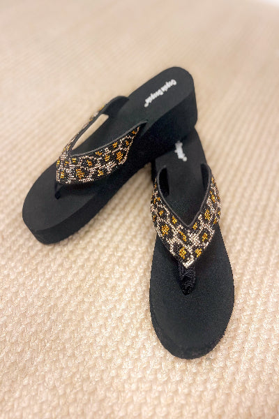 Black flip-flops with decorative straps on a beige surface