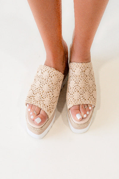 Beige open-toe sandals with textured sole worn by a person on a light background